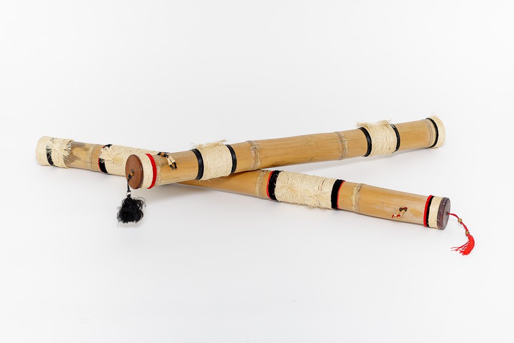 Two handmade bamboo fly fishing rod cases crossed over each other, featuring black and red painted bands, cream rope wrappings, and wooden caps with tassels on a white background.